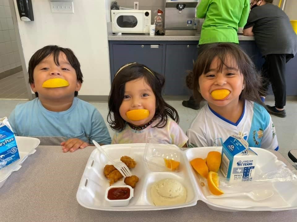 3 head start students eating lunch with oragne slice smiles