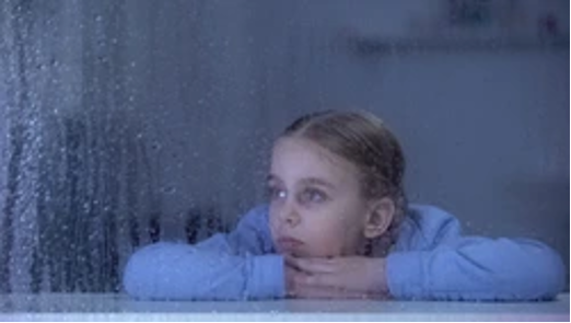 Child staring out window on rainy day