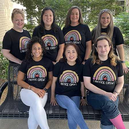 The Skaggs 2022-2023 Office Staff smiling around a bench in their black Skaggs Office Team shirts.
