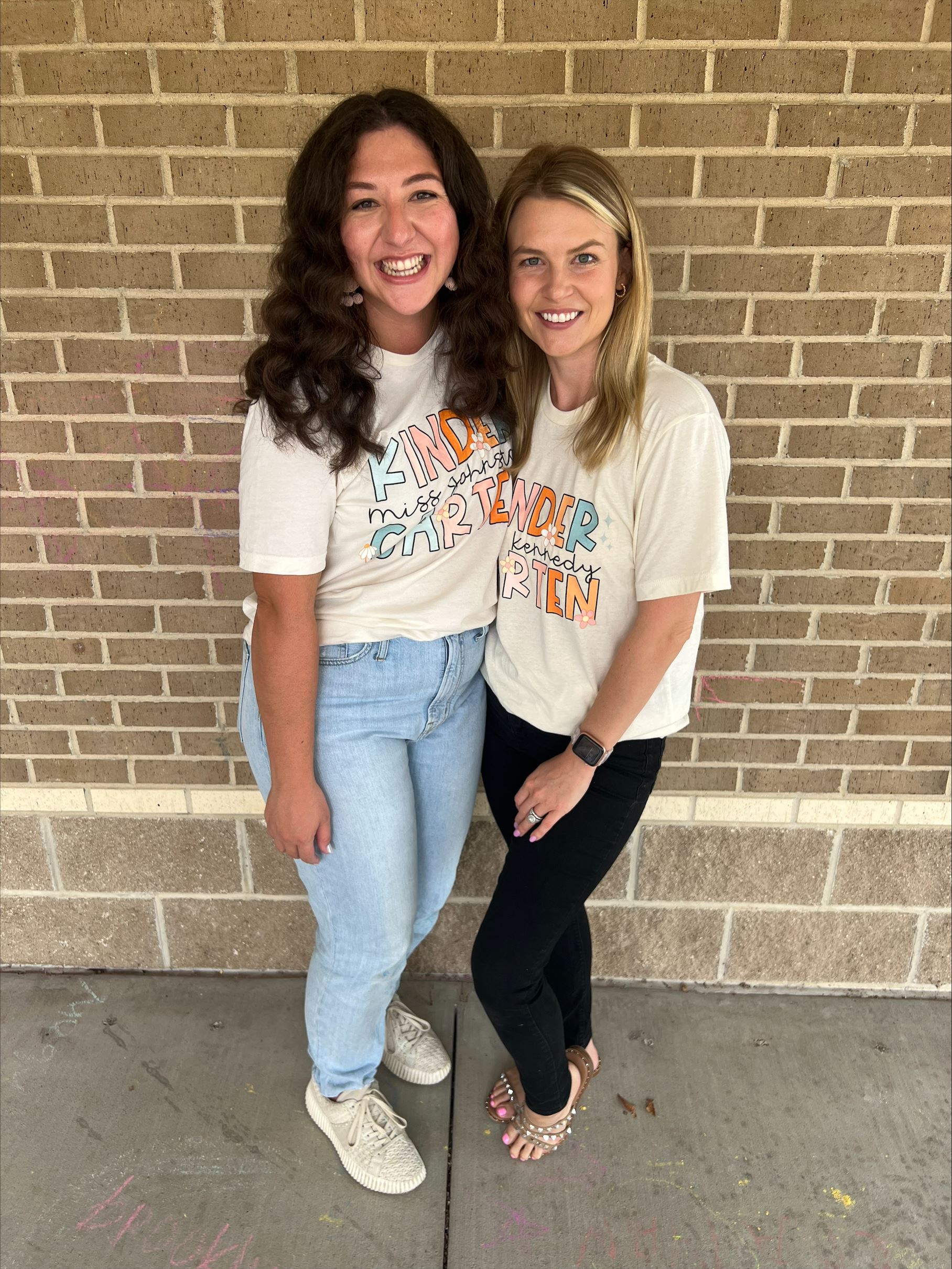 Mrs. Johnston and Mrs. Kennedy wearing their Skaggs team shirts and smiling in front of a brick wall.