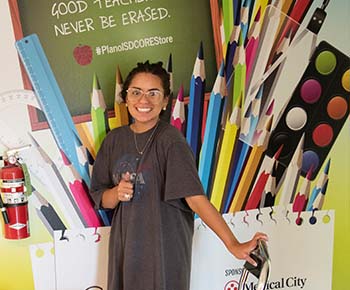  teacher giving thumbs up in front of mural of pencils and supplies