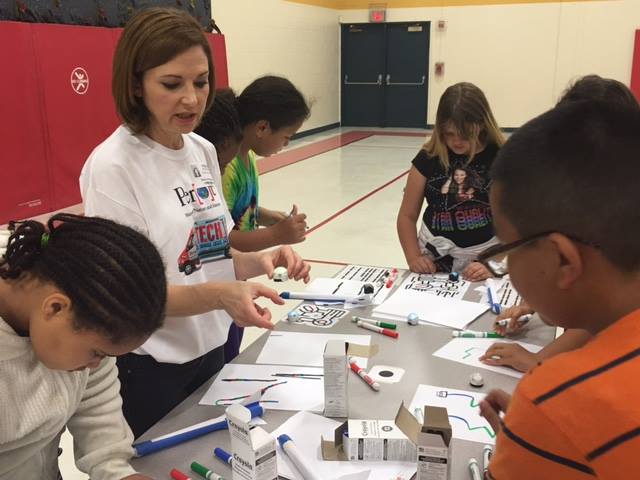 woman volunteer helping table of students using markers 