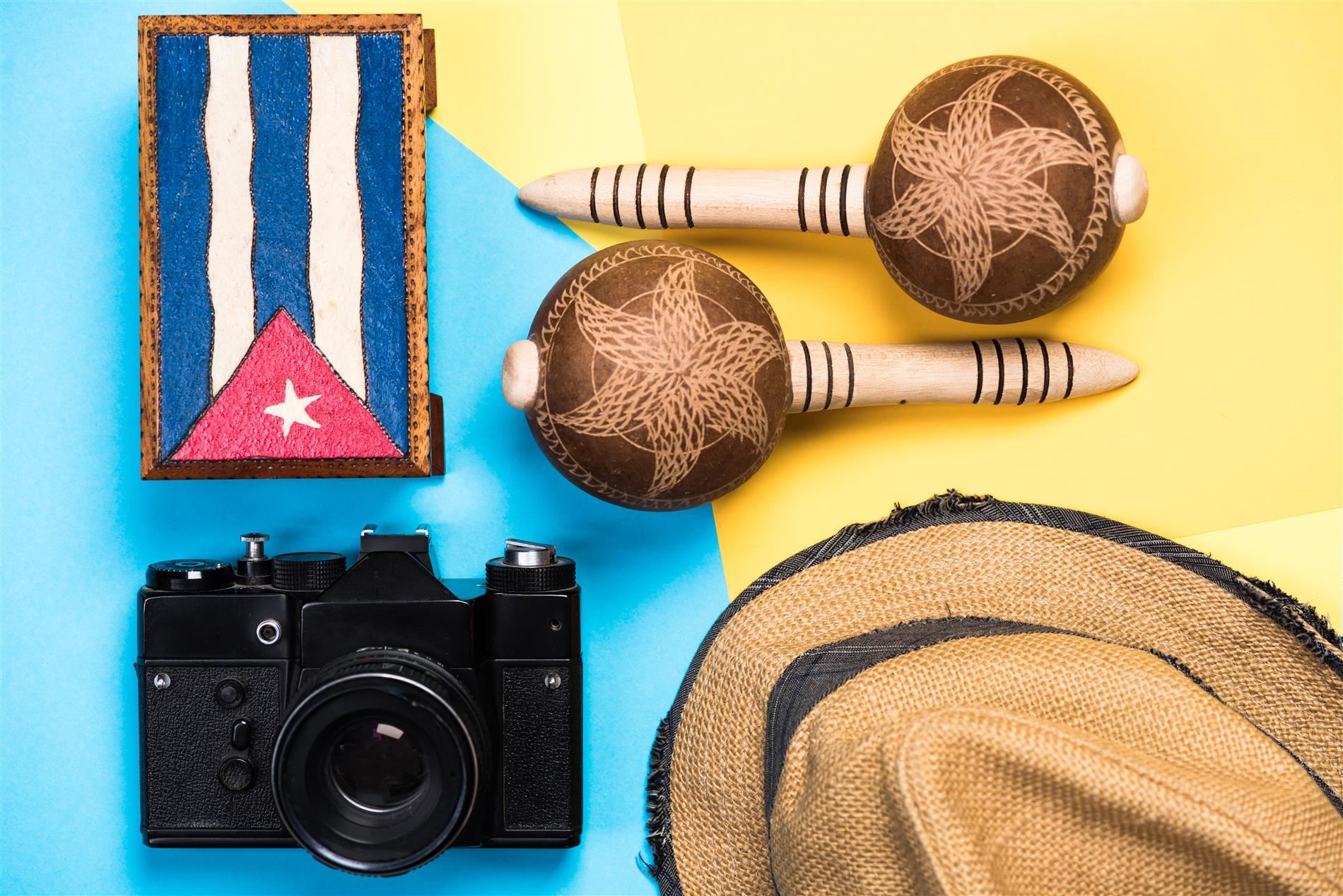 Various items arranged on a multicolored surface including a flag from Puerto Rico, a camera, a hat and maracas.