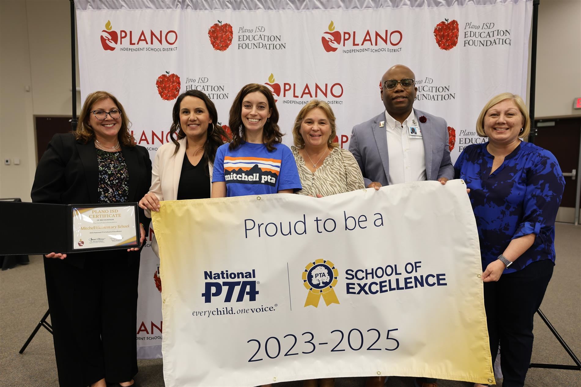 Multiple individuals standing behind a PTA School of Excellence banner
