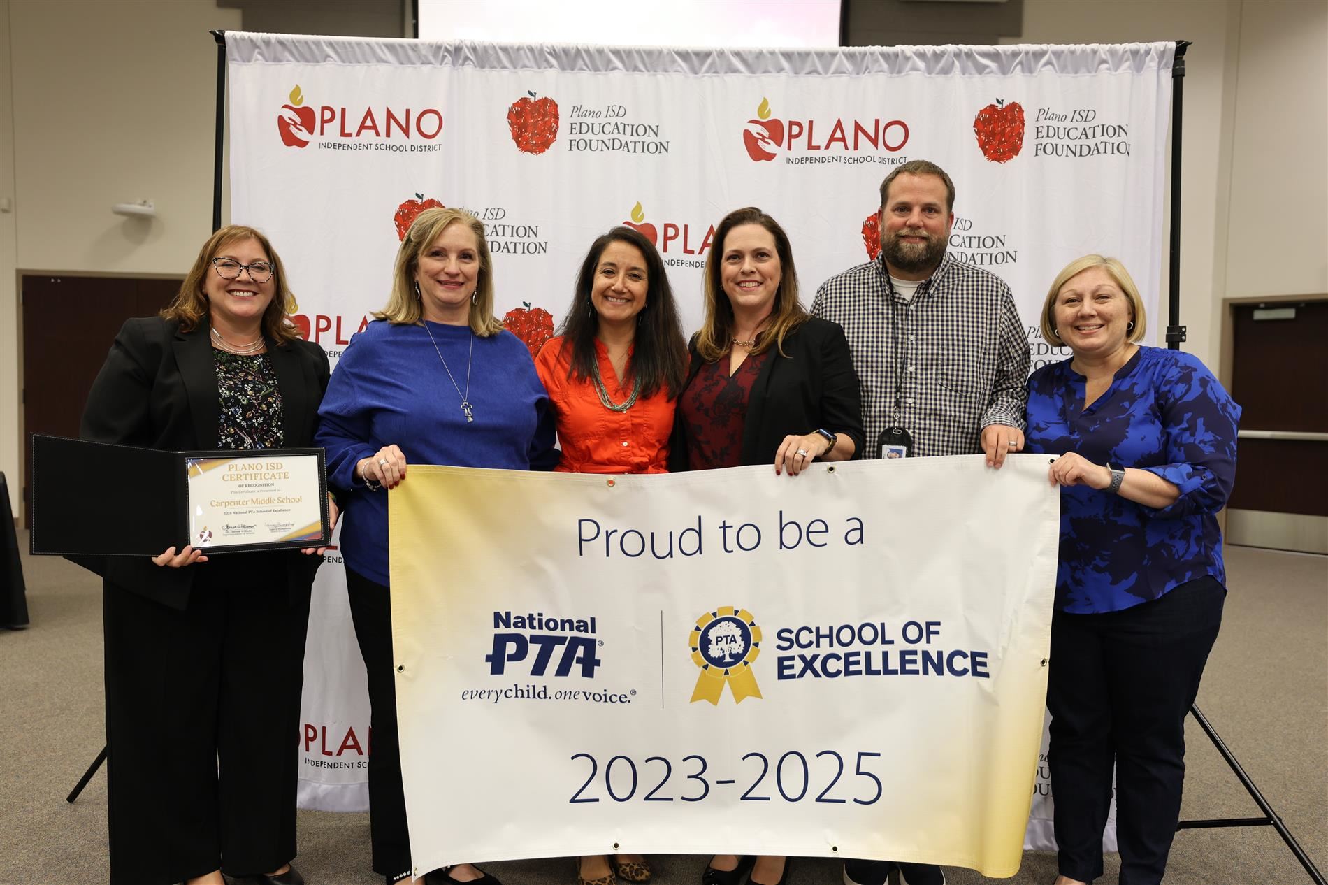 Multiple individuals standing behind a PTA School of Excellence banner