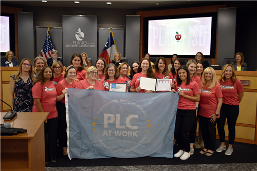 Harrington Elementary staff posing with PLC banner and board recognition certificate