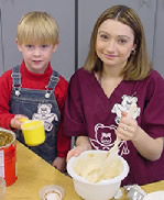 Preschool student aide making cookies with young child 