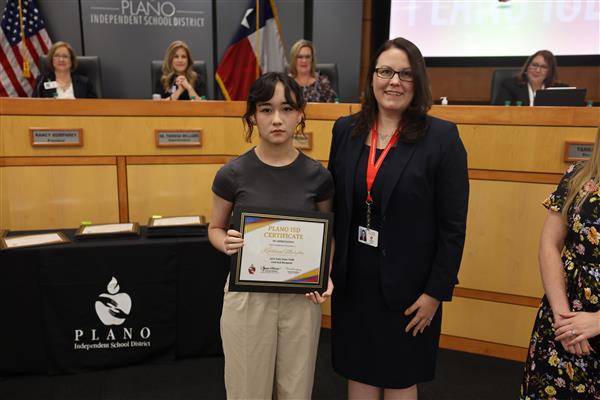 two individuals posing in front of the Plano ISD Board dais