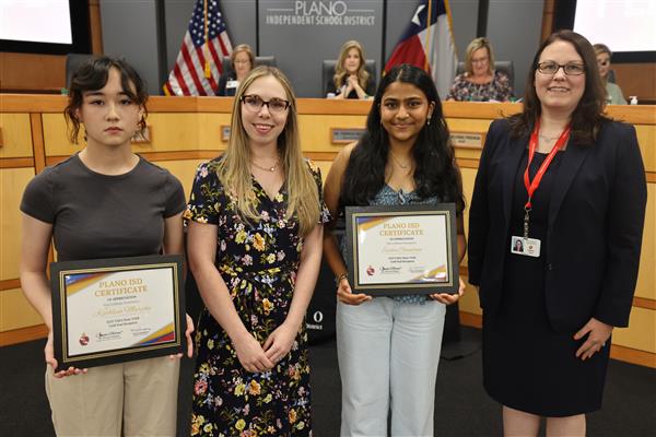 two individuals posing in front of the Plano ISD Board dais