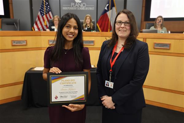 two individuals posing in front of the Plano ISD Board dais