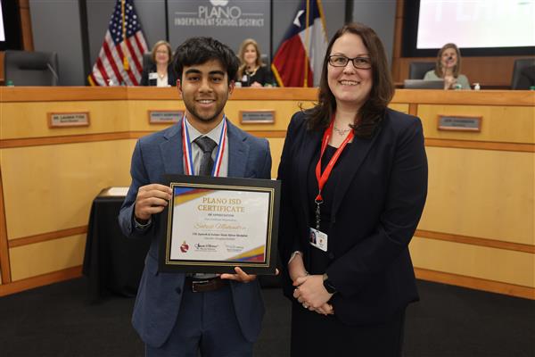 two individuals posing in front of the Plano ISD Board dais