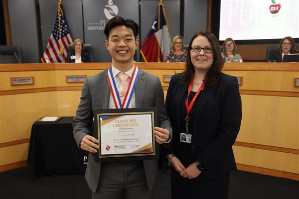 two individuals posing in front of the Plano ISD Board dais