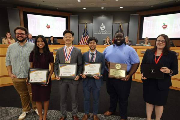 multiple individuals posing in front of the Plano ISD Board dais