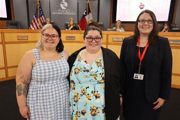 Three individuals posing in front of the Plano ISD Board Dais
