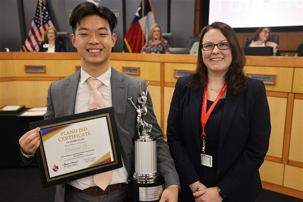 Two individuals posing in front of the Plano ISD Board Dais