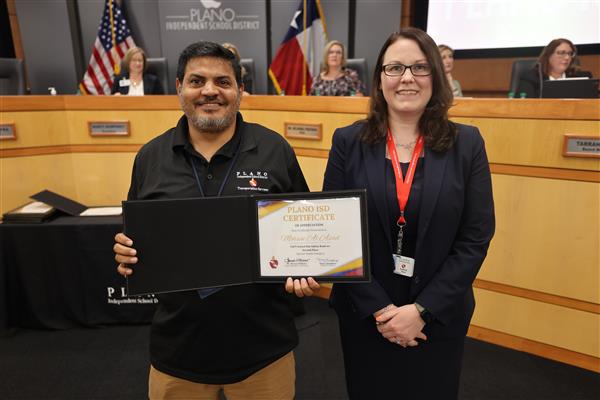 Two individuals posing in front of the Plano ISD Board Dais