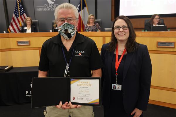 Two individuals posing in front of the Plano ISD Board Dais