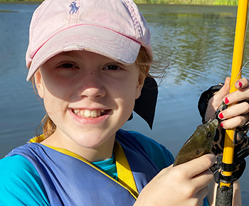 Elementary girl with fishing pole and a fish she caught at camp